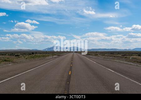 Nevadas Frühlingslandschaft mit Wüstenstraße, die zu fernen Bergen unter teilweise bewölktem Himmel mit Sonnenaufgang und blauen Akzenten führt. Stockfoto