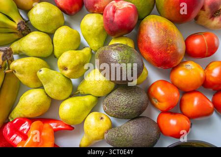 Minimalistisches Stillleben, wo Bananen, Birnen, Avocados, Kartoffeln, Nektarinen, und Feigen erzeugen einen Regenbogen aus Farben auf einem blassblauen Hintergrund Stockfoto