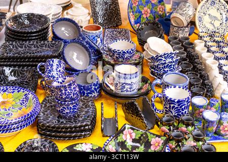 Ein Tisch voller blauer und weißer Tassen. Die Tabelle ist gelb. Die Gerichte sind bunt und mit Blumen bedruckt. Stadt Puebla, Mexiko, Kunsthandwerk Stockfoto