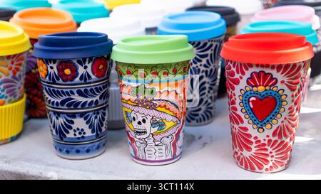 Eine Reihe farbenfroher Kaffeetassen mit Motiven. Die Becher sind in einer Reihe angeordnet, wobei einige größer sind als andere. Die Tassen sind mit V verziert Stockfoto