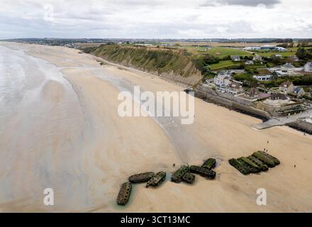 Bei Ebbe spazieren die Menschen am Strand von Arromanches-les-Bains, Normandie, Frankreich, um die Überreste von Mulberry Harbour herum Stockfoto