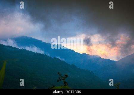 Atemberaubende Aussicht auf die nebelbedeckten Berge bei Sonnenaufgang, mit dramatischen Wolken und leuchtenden Orangetönen, die eine ruhige und dennoch kraftvolle Atmosphäre schaffen Stockfoto