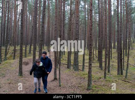 Kleine Figuren von Mann und Kind, die an einem bewölkten Tag in einem hohen Kiefernwald spazieren gehen Stockfoto