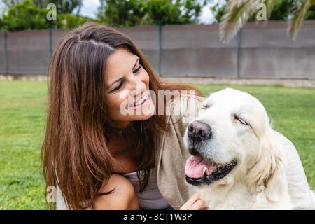 Frau lacht, während sie draußen ihren glücklichen goldenen Retriever streichelt. Lifestyle. Tiere. Stockfoto