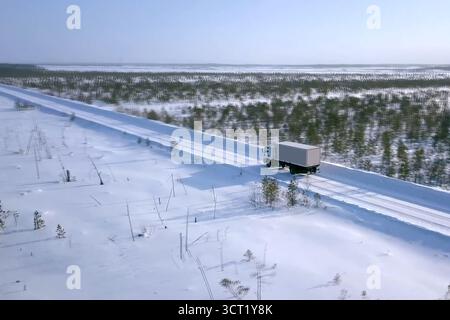 Im Winter fährt ein Lastwagen mit einem Wagen auf der Straße. Winterstraße für einen Lastwagen. Stockfoto
