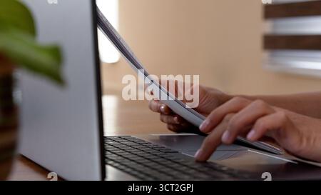 Person, die in einem gemütlichen Café mit Büchern und einer Tasse Kaffee auf einem Laptop tippt Stockfoto