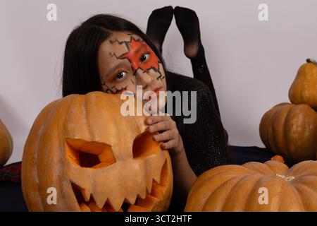 Mädchen mit Kürbis Gesichtsfarbe in einem Halloween-Kostüm, das hell gegen sie lächelt Stockfoto