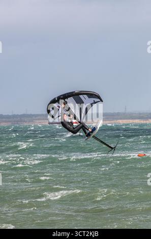 Ein Mann, der einen Taucheranzug trägt, der auf einer Flügelfolie auf einer rauen See und einem windigen Tag auf dem Solent vor Cowes auf der isle of wight Luft bekommt. Stockfoto
