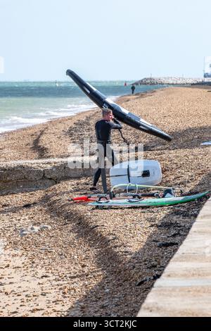 Mann, der einen Taucheranzug trägt, mit zwei Flügelschweinen an einem Kieselstrand, der sich darauf vorbereitet, ins Meer zu gelangen. Stockfoto
