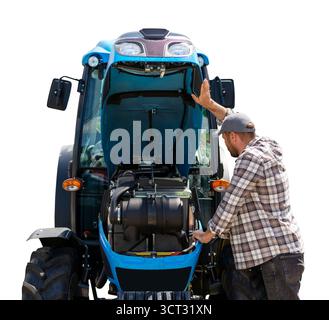 Männlicher Mechaniker, der den Traktor mit geöffnetem Hufhufe inspiziert. Stockfoto