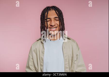 Eine junge Person mit geflochtenen Haaren und Spangen lächelt glücklich. Sie tragen ein helles Hemd und stehen vor einem rosa Hintergrund, s Stockfoto