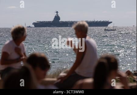 Palma, Spanien. Oktober 2025. Die Menschen sitzen am Strand von Can Pere Antoni, während der US-Flugzeugträger USS Gerald R. Ford in der Bucht von Palma vor Anker liegt. Das größte und modernste Kriegsschiff der US Navy ist gestern auf Mallorca angekommen und soll bis zum 8. Oktober bleiben. Quelle: Clara Margais/dpa/Alamy Live News Stockfoto