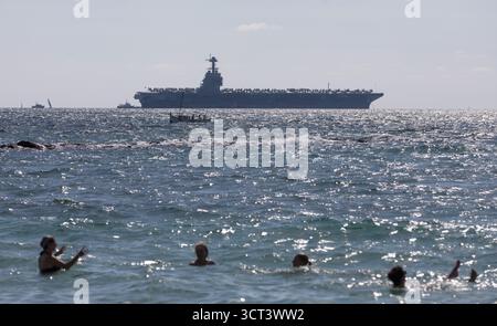 Palma, Spanien. Oktober 2025. Die Menschen baden am Strand von Can Pere Antoni, während der US-Flugzeugträger USS Gerald R. Ford in der Bucht von Palma vor Anker liegt. Das größte und modernste Kriegsschiff der US Navy ist gestern auf Mallorca angekommen und soll bis zum 8. Oktober bleiben. Quelle: Clara Margais/dpa/Alamy Live News Stockfoto