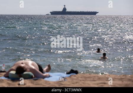 Palma, Spanien. Oktober 2025. Menschen am Strand von Can Pere Antoni, während der US-Flugzeugträger USS Gerald R. Ford in der Bucht von Palma vor Anker liegt. Das größte und modernste Kriegsschiff der US Navy ist gestern auf Mallorca angekommen und soll bis zum 8. Oktober bleiben. Quelle: Clara Margais/dpa/Alamy Live News Stockfoto