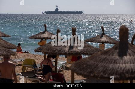 Palma, Spanien. Oktober 2025. Menschen am Strand von Can Pere Antoni, während der US-Flugzeugträger USS Gerald R. Ford in der Bucht von Palma vor Anker liegt. Das größte und modernste Kriegsschiff der US Navy ist gestern auf Mallorca angekommen und soll bis zum 8. Oktober bleiben. Quelle: Clara Margais/dpa/Alamy Live News Stockfoto