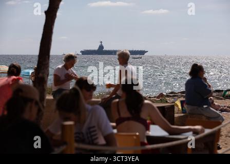 Palma, Spanien. Oktober 2025. Menschen am Strand von Can Pere Antoni, während der US-Flugzeugträger USS Gerald R. Ford in der Bucht von Palma vor Anker liegt. Das größte und modernste Kriegsschiff der US Navy ist gestern auf Mallorca angekommen und soll bis zum 8. Oktober bleiben. Quelle: Clara Margais/dpa/Alamy Live News Stockfoto