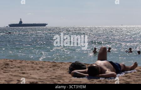 Palma, Spanien. Oktober 2025. Menschen am Strand von Can Pere Antoni, während der US-Flugzeugträger USS Gerald R. Ford in der Bucht von Palma vor Anker liegt. Das größte und modernste Kriegsschiff der US Navy ist gestern auf Mallorca angekommen und soll bis zum 8. Oktober bleiben. Quelle: Clara Margais/dpa/Alamy Live News Stockfoto