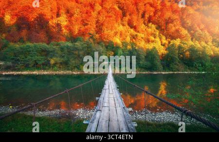 Hölzerne Hängebrücke über einen ruhigen Fluss und Herbstwald Stockfoto