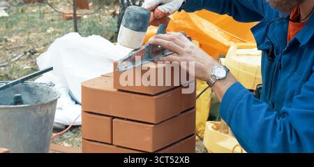 Ein Mann baut eine Ziegelmauer. Backstein auf die Lösung. Bau eines Ziegelhauses. Stockfoto