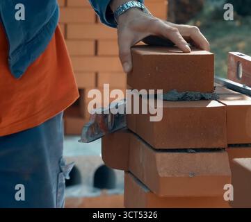 Ein Mann baut eine Ziegelmauer. Backstein auf die Lösung. Bau eines Ziegelhauses. Stockfoto