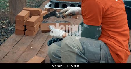 Ein Mann baut eine Ziegelmauer. Backstein auf die Lösung. Bau eines Ziegelhauses. Stockfoto