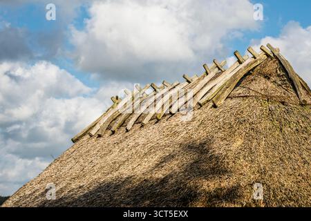Nahaufnahme des Wikinger-Langhauses mit Strohdach mit Holzkappen und wolkenbewölktem Herbsthimmel. Stockfoto