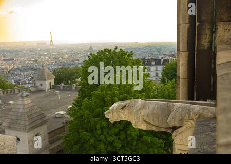 Dieses Foto zeigt einen Gargoyle auf einem Gebäude mit Blick auf die Skyline von Paris, während der Eiffelturm in der Ferne bei Sonnenuntergang oder Sonnenris sichtbar ist Stockfoto