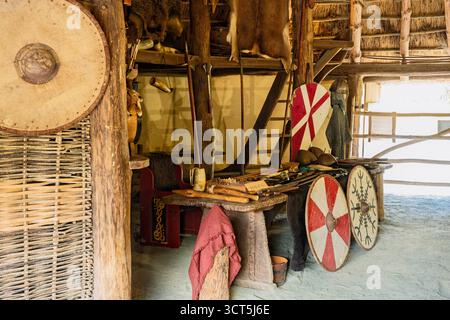 Das Innere des Viking Longhouse zeigt Schilde, Äxte und Pelze auf Holztisch, Wexford, Irish National Heritage Park Stockfoto