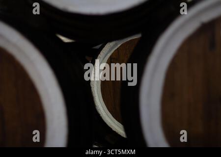 Nahaufnahme, selektiver Fokus auf einem hölzernen Fassende, teilweise durch andere Fässer verdeckt, in einem dunklen Keller. Stockfoto