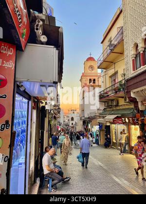 Historische Kirche mit roter Kuppel und Uhrenturm mit Blick auf die pulsierende Straßenszene in Tangiers Old Medina Kasbah, Marokko. Vom 3. Oktober 2025 Stockfoto