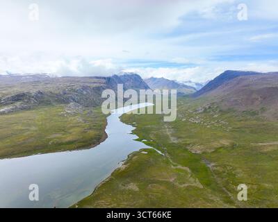 Weite Sicht aus der Luft auf einen langen, geschwungenen See und Fluss in einem breiten, hochgelegenen grünen Tal, umgeben von felsigen, wolkenbedeckten Bergen Stockfoto