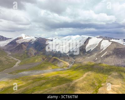 Weite Luftaufnahme eines Gebirges mit ausgedehnten Schneefeldern und Gletschern, die ein System von Schmelzwasserflüssen im Vordergrund speisen Stockfoto