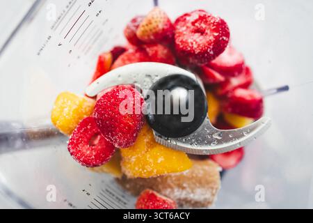 Ein Schuss gefrorener Erdbeeren, Bananen und Mango in einem Mixer, fertig zum Mixen. Gesundes Lifestyle-Thema, bunte Szene mit natürlichem Licht Stockfoto