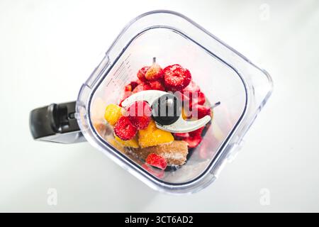 Ein Schuss gefrorener Erdbeeren, Bananen und Mango in einem Mixer, fertig zum Mixen. Gesundes Lifestyle-Thema, bunte Szene mit natürlichem Licht Stockfoto