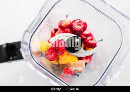 Ein Schuss gefrorener Erdbeeren, Bananen und Mango in einem Mixer, fertig zum Mixen. Gesundes Lifestyle-Thema, bunte Szene mit natürlichem Licht Stockfoto