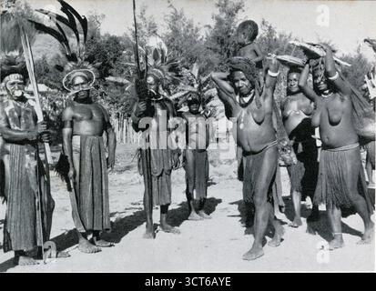 Vintage 1960er Jahre Foto von Chimbu-Frauen, die abends aus ihren Gärten kommen, mit Süßkartoffeln, Männer in zeremonieller Kostümuhr. Die Chimbu sind ein isolierter Stamm in Papua-Neuguinea, insbesondere aus der Provinz Chimbu (oder Simbu) in der bergigen zentralen Highlands-Region des Landes, Papua-Neuguinea 1964 Stockfoto