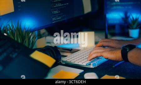 Programmierer Arbeitsbereich Nachtcodierung Monitor Tastatur Haftnotizen. Nahaufnahme von Entwicklerhänden, die in dunklen Büros auf der Tastatur mit Quellcode auf scr tippen Stockfoto