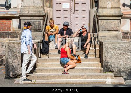 Junge Erwachsene genießen Getränke auf der Treppe der ENSI Linja 1 während des Straßenfestes Kallio Block Party 2025 im Bezirk Kallio in Helsinki, Finnland Stockfoto