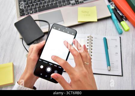 Nahaufnahme weiblicher Hände, die ein Mobiltelefon mit leerem Bildschirm in einer Büroumgebung halten Stockfoto