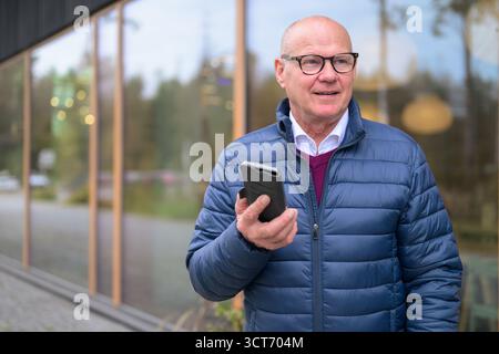 Porträt eines älteren skandinavischen Mannes, der ein Handy in der Stadt benutzt Stockfoto