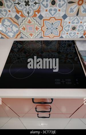 Modernes schwarzes Induktionskochfeld in einer Küche mit marokkanischen Fliesen. Nahaufnahme des eingebauten Elektroherds auf der Arbeitsplatte mit dekorativem ce Stockfoto