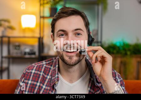 Rufen Sie mich an. Glücklicher kaukasischer Mann, der zu Hause auf der Couch sitzt, Headset trägt, freiberuflicher Mitarbeiter, Callcenter, Support Service Operator Helpline, spricht mit Stockfoto