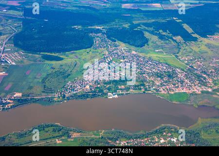 Luftbild zeigt die Stadt an einem See, umgeben von grünen Feldern und Wäldern, die eine Mischung aus städtischen und natürlichen Landschaften unter weitem Himmel hervorheben. Ruhig Stockfoto
