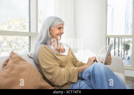 Fröhliche, reife Hausbesitzerin, die soziale Medien auf dem Tablet durchsucht Stockfoto