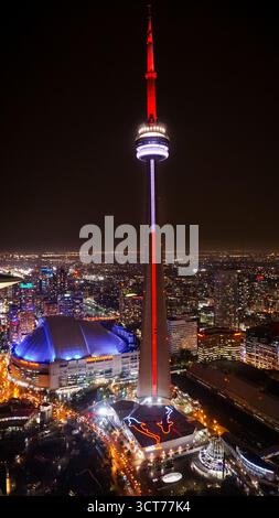 Nächtlicher Blick auf den CN Tower, beleuchtet in roten und weißen Lichtern, mit Blick auf die Innenstadt von Toronto mit dem Rogers Centre, das in Blau leuchtet. Stockfoto