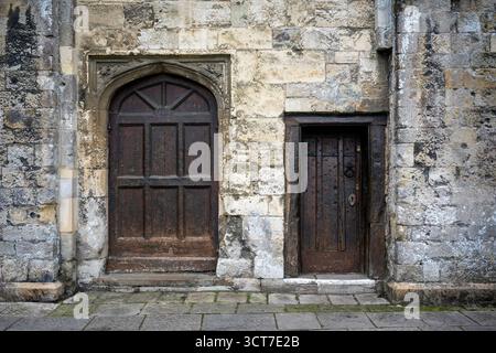 Verwitterte Steinmauer mit einer großen Bogentür und einer kleineren Holztür Stockfoto