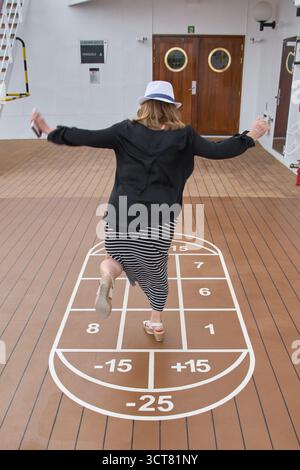 Viladecans. Spanien - 03. Oktober 2025: Eine Frau mit Hut balanciert ihren Körper aus, während sie zwischen den Zahlen eines Bodenspiels springt und die Freude und das Spiel einfängt Stockfoto