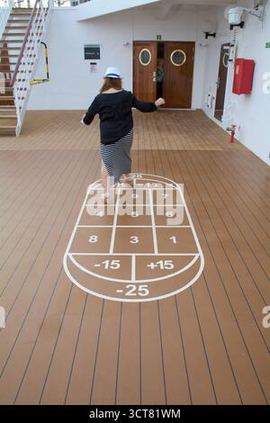 Viladecans. Spanien - 03. Oktober 2025: Eine Frau, die von hinten auf einem Bein gesehen wird, während sie ein Deckspiel auf einem Kreuzfahrtschiff spielt und einen Moment der Pflege zeigt Stockfoto