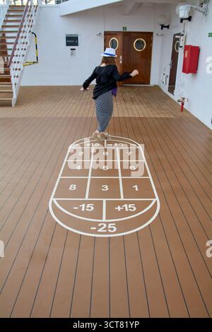 Viladecans. Spanien - 03. Oktober 2025: Eine Frau mit Hut nimmt an einem Bodenspiel auf einem Kreuzfahrtschiff Teil und zeigt einen aktiven und gesunden Lebensstil Stockfoto