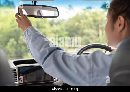 Frau verstellt den Rückspiegel vor der Fahrt, fährt mit Absicht, sichere Fahrt, Fahrpraxis, fröhliche Frau sitzt bequem auf dem Fahrersitz wi Stockfoto